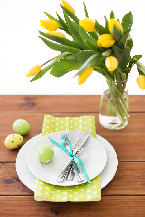 easter, holidays, tradition and object concept - green colored egg, plates with cutlery and tulip flowers on table at home