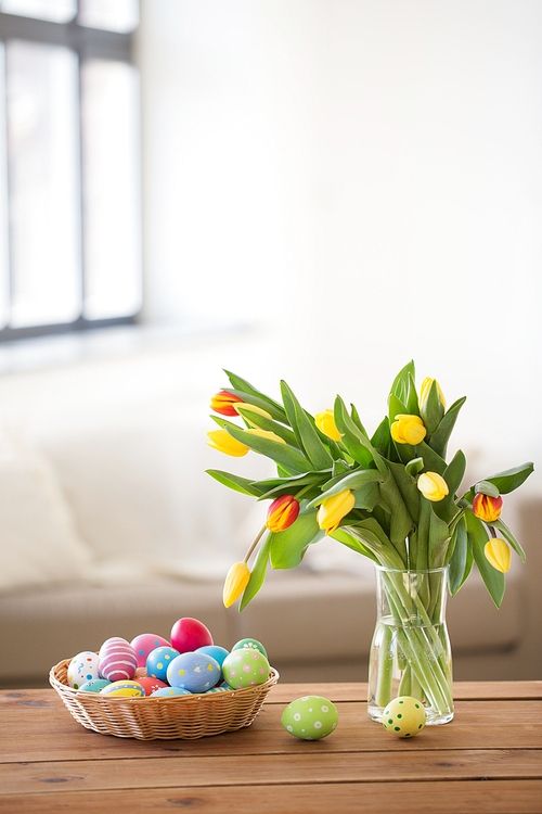 easter, holidays, tradition and object concept - colored eggs in basket and tulip flowers at home