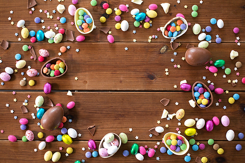 easter, sweets and confectionery concept - chocolate eggs and candy drops on wooden background