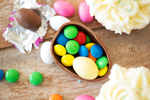 easter, food and holidays concept - half of chocolate egg with candies and cupcakes wooden on table