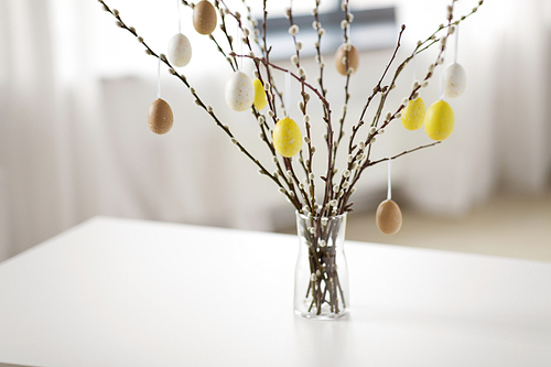 holidays and object concept - pussy willow branches decorated by easter eggs in vase on table