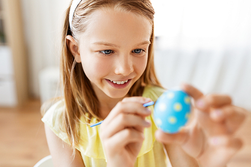 easter, holidays and people concept - happy girl coloring egg with colors and brush at home