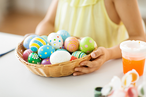 easter, holidays and people concept - close up of girl with colored eggs in wicker basket