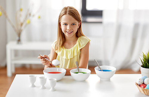 easter, holidays and people concept - happy girl coloring eggs by liquid dye at home