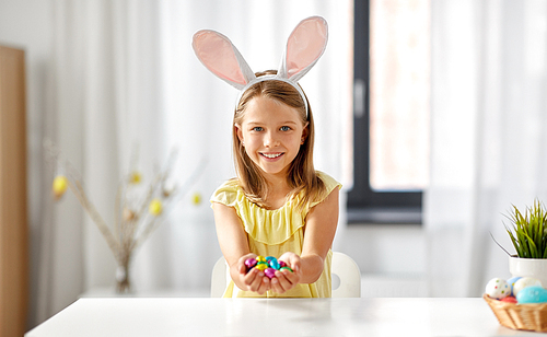 easter, holidays and people concept - happy girl wearing bunny ears headband with chocolate eggs at home