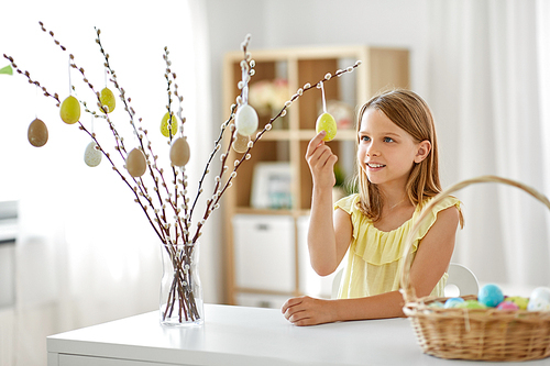 easter, holidays and people concept - happy girl decorating willow branches by toy eggs at home