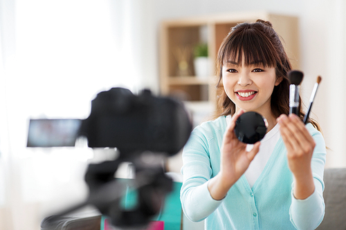 blogging, technology, videoblog and people concept - happy smiling asian beauty . with camera, brushes and blush recording video blog about make up and cosmetics at home