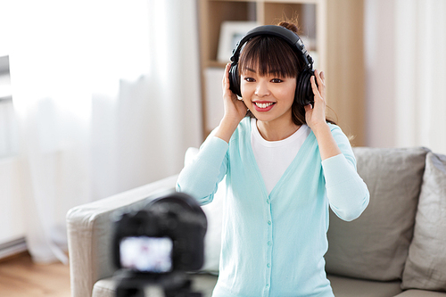 blogging, videoblog and people concept - asian female . with camera recording video review of headphones at home