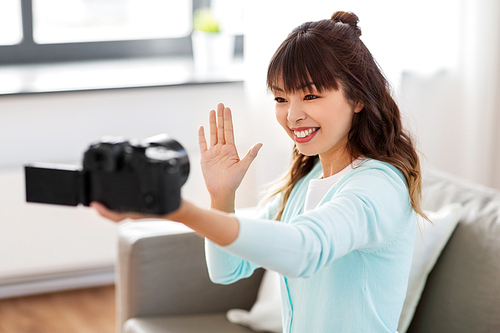 blogging, videoblog and technology concept - asian woman or . with camera recording video blog or taking selfie and waving hand at home
