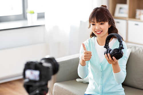 blogging, videoblog and people concept - asian female . with camera recording video review of headphones and showing thumbs up gesture at home