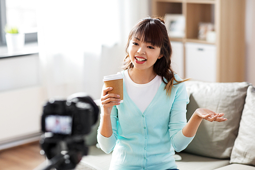 blogging, technology, videoblog and people concept - nice asian woman or . with camera and takeaway coffee cup recording video blog at home in morning