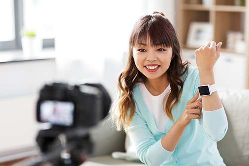 blogging, technology and videoblog concept - happy smiling asian woman or . with camera recording video blog of smart watch at home