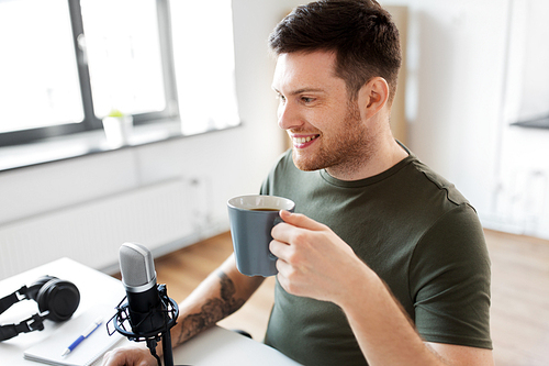 technology, mass media and podcast concept - happy male audio . with microphone drinking coffee and broadcasting at home office