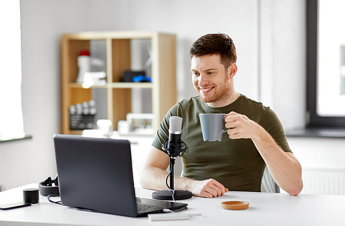 technology, mass media and podcast concept - happy male audio . with laptop computer and microphone drinking coffee and broadcasting at home office