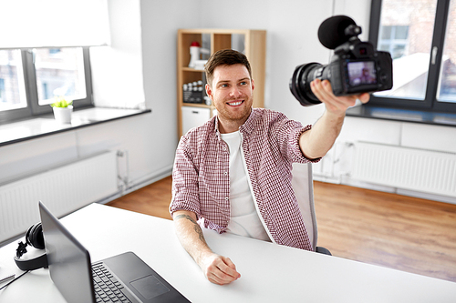 blogging, videoblog and people concept - male . holding camera and recording video blog at home office