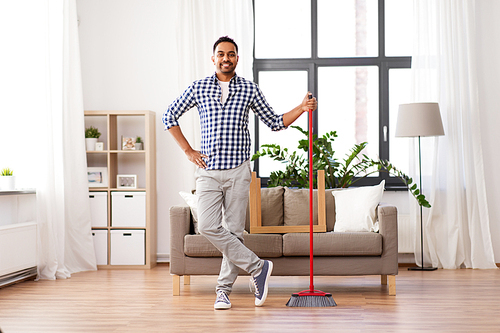 cleaning, housework and housekeeping concept - smiling indian man with broom at home