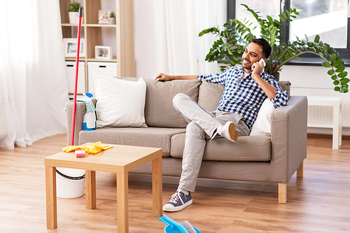 household and technology concept - happy indian man calling on smartphone after cleaning home