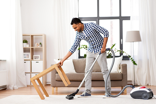 household and cleaning concept - indian man with vacuum cleaner at home