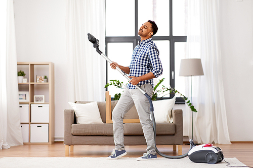 household and cleaning concept - indian man with vacuum cleaner having fun at home