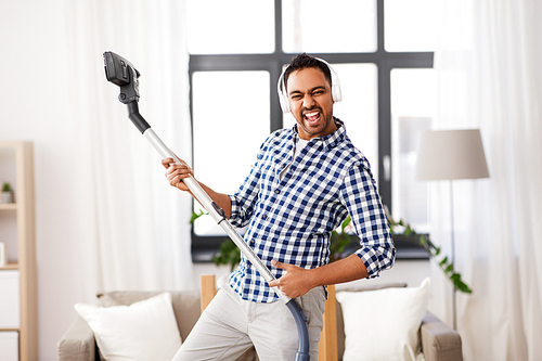 household and cleaning concept - indian man in headphones with vacuum cleaner having fun at home