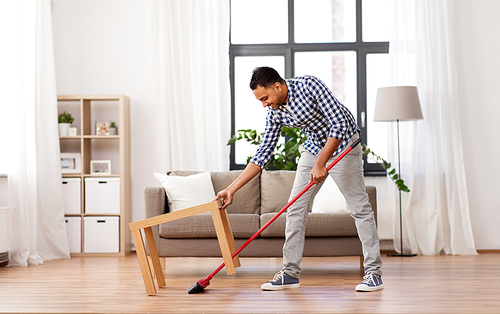 cleaning, housework and housekeeping concept - indian man with broom sweeping floor at home