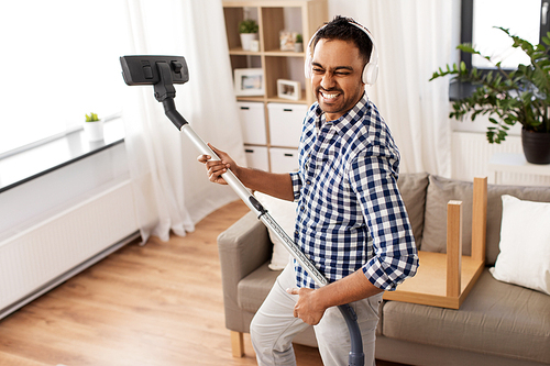 household and cleaning concept - indian man in headphones with vacuum cleaner having fun at home