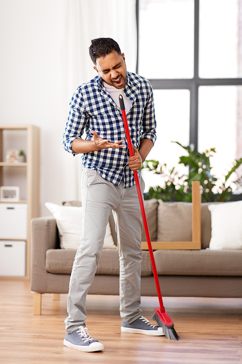 cleaning, housework and housekeeping concept - indian man with broom sweeping floor and singing at home