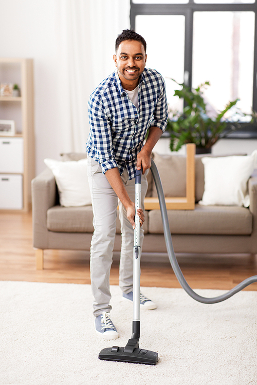 household and cleaning concept - indian man with vacuum cleaner at home