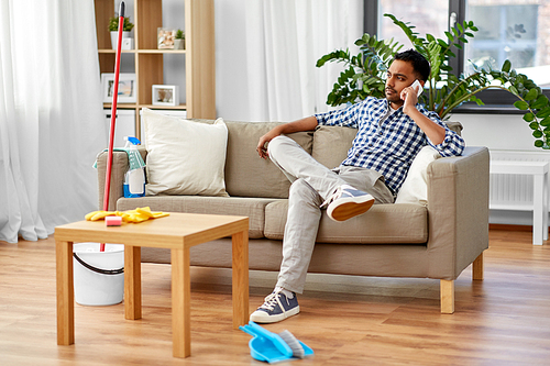 household and technology concept - indian man calling on smartphone after cleaning home