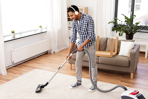 household and cleaning concept - indian man in headphones with vacuum cleaner at home