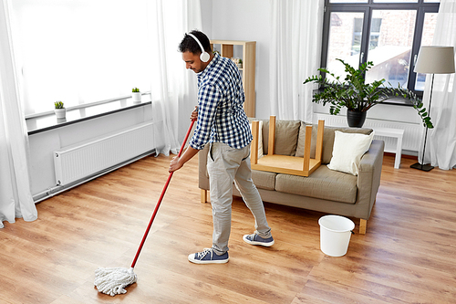 household, housework and people concept - happy indian man in headphones with mop and bucket cleaning floor and listening to music at home