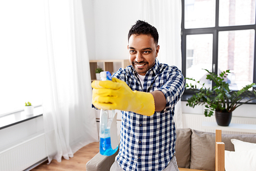 cleaning, housework and housekeeping concept - smiling indian man in protective rubber gloves shooting with detergent at home