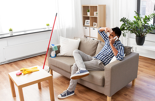 household and technology concept - tired indian man calling on smartphone after cleaning home