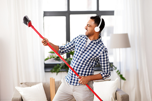 cleaning, housework and housekeeping concept - indian man in headphones with broom sweeping and having fun at home