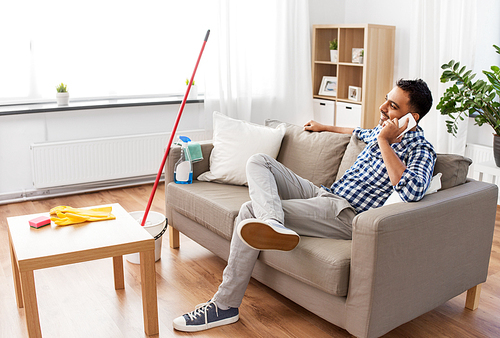 household and technology concept - happy indian man calling on smartphone after cleaning home