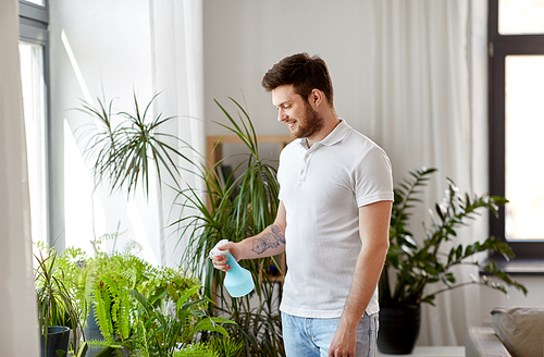 people, nature and plants care concept - man spraying houseplants by water sprayer at home