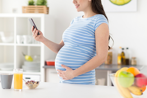 pregnancy, healthy eating and maternity concept - close up of pregnant woman with breakfast on kitchen table using smartphone and touching her belly at home