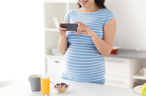 pregnancy, healthy eating and maternity concept - close up of pregnant woman with smartphone touching her belly with breakfast on kitchen table at home