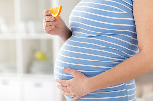pregnancy, healthy food and people concept - close up of pregnant woman eating orange at home
