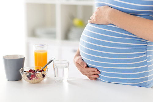 pregnancy, healthy eating and maternity concept - close up of pregnant woman with breakfast on kitchen table touching her belly at home