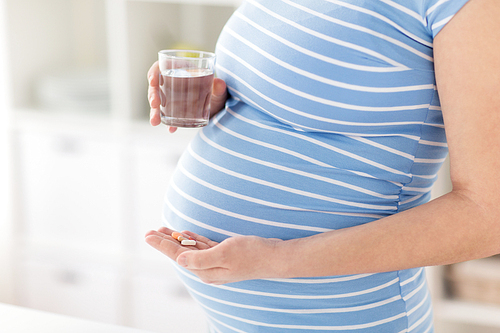 pregnancy, people and health care concept - close up of pregnant woman with vitamin pills and glass of water