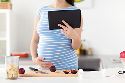 cooking, pregnancy and technology concept - pregnant woman with tablet computer, kitchen knife and plums on wooden cutting board at home