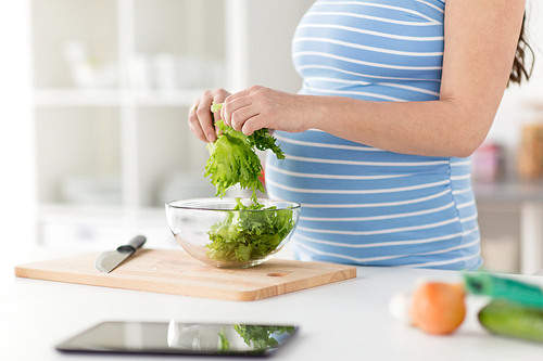 pregnancy, cooking food and healthy eating concept - close up of pregnant woman chopping lettuce by hands for salad at home kitchen
