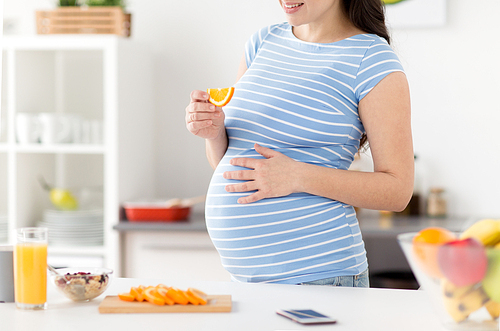 pregnancy, healthy food and people concept - close up of pregnant woman eating orange for breakfast at home kitchen