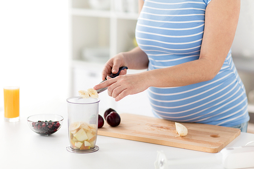 cooking, pregnancy and healthy eating concept - pregnant woman with kitchen knife chopping fruits at home