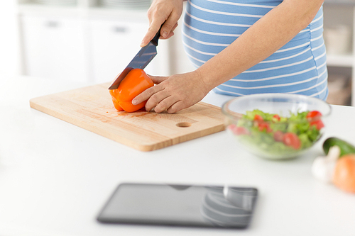 pregnancy, cooking food and healthy eating concept - close up of pregnant woman making vegetable salad and chopping pepper by kitchen knife on cutting board at home kitchen