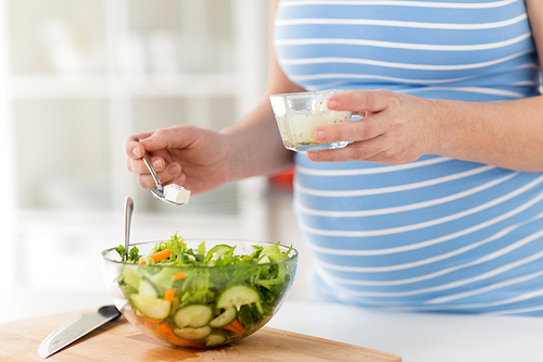 pregnancy, cooking food and healthy eating concept - close up of pregnant woman making vegetable salad and adding feta cheese at home kitchen