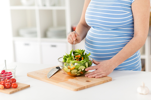 pregnancy, cooking food and healthy eating concept - close up of pregnant woman making vegetable salad at home kitchen