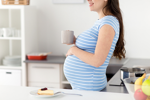 pregnancy, people and expectation concept - close up of pregnant woman with cup of tea at home kitchen