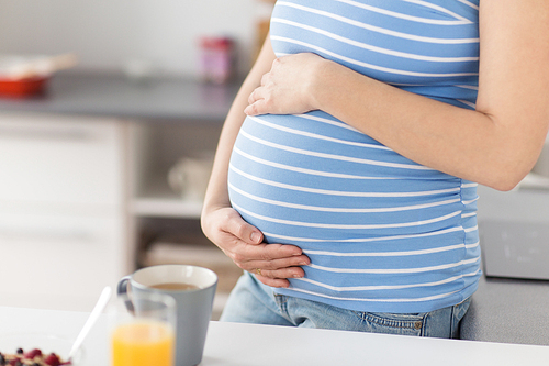 pregnancy, maternity and expectation concept - close up of pregnant woman touching her belly at home kitchen